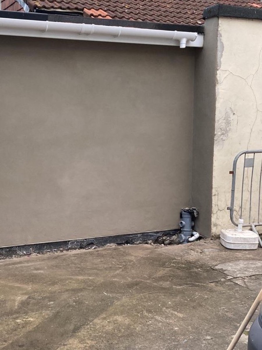 The same extension wall finished in smooth grey render, guttering on and the site cleared