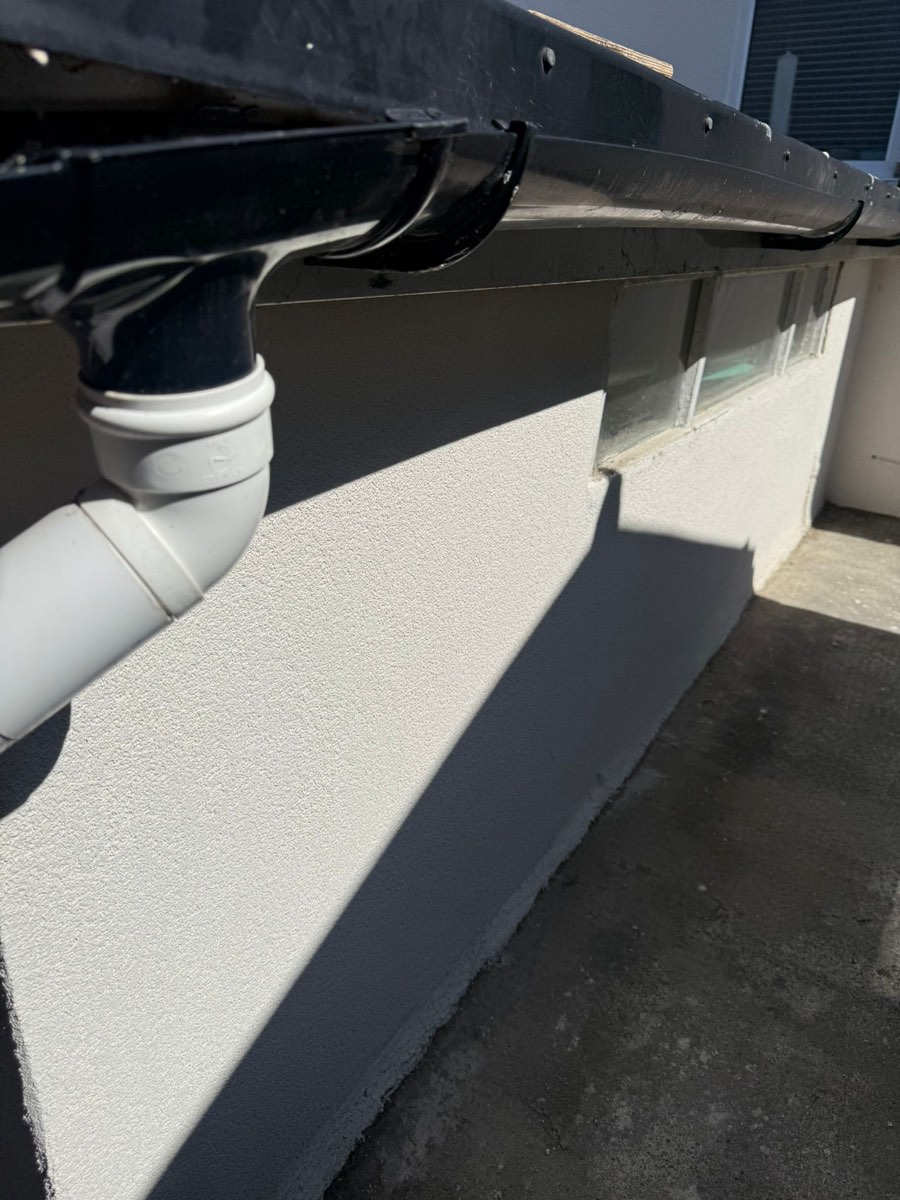 Close detail of white textured render meeting a dark grey plinth in a clean straight line below black guttering