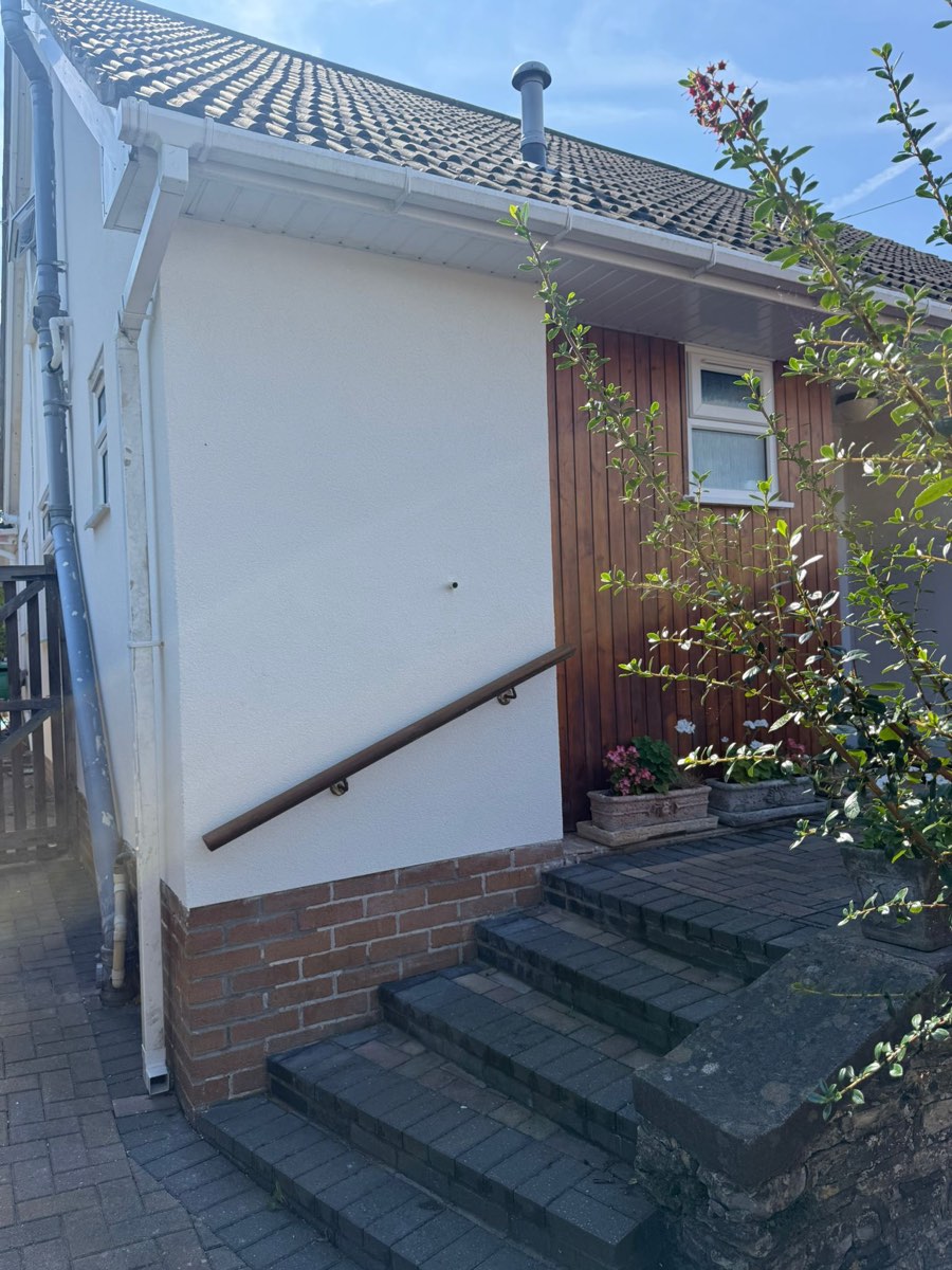 The same entrance after rendering, crisp white walls cut in around the timber door, handrail and brick steps