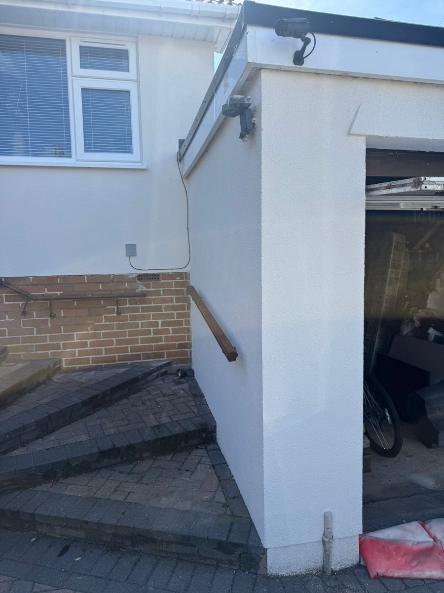 Freshly rendered wall beside a carport, cut in cleanly against brickwork and a timber handrail