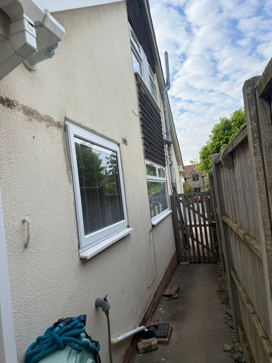 A narrow side passage before work, patched and stained cream render below dark timber boarding