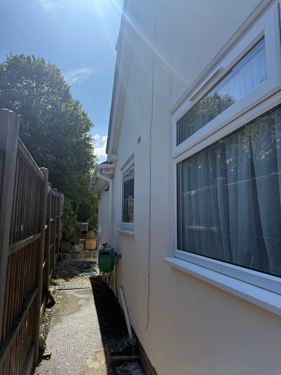 A rendered side elevation in bright sunshine, smooth white walls beside a timber fence