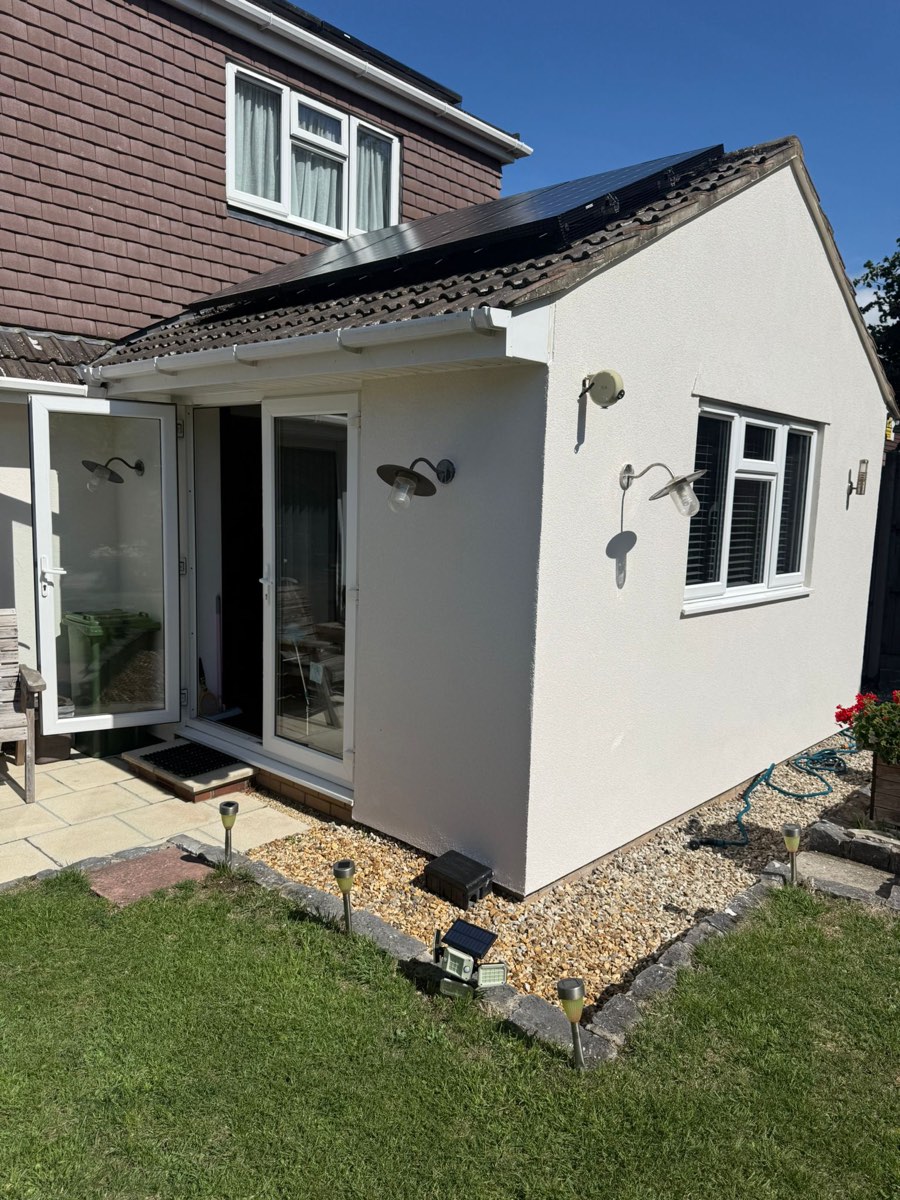 A newly rendered single-storey garden room in white render with wall lights and a gravel border