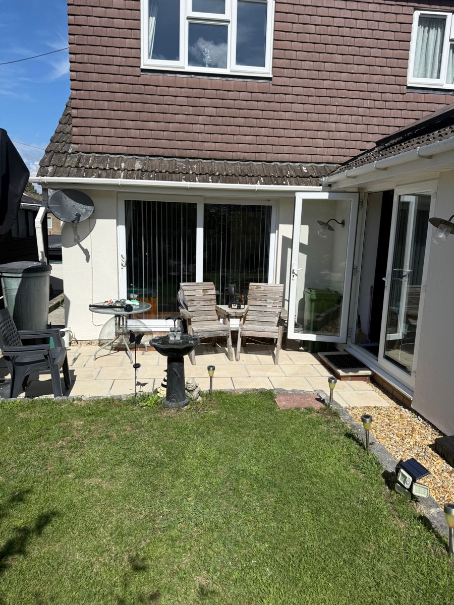 A rendered house elevation seen from the lawn, patio and garden furniture in front