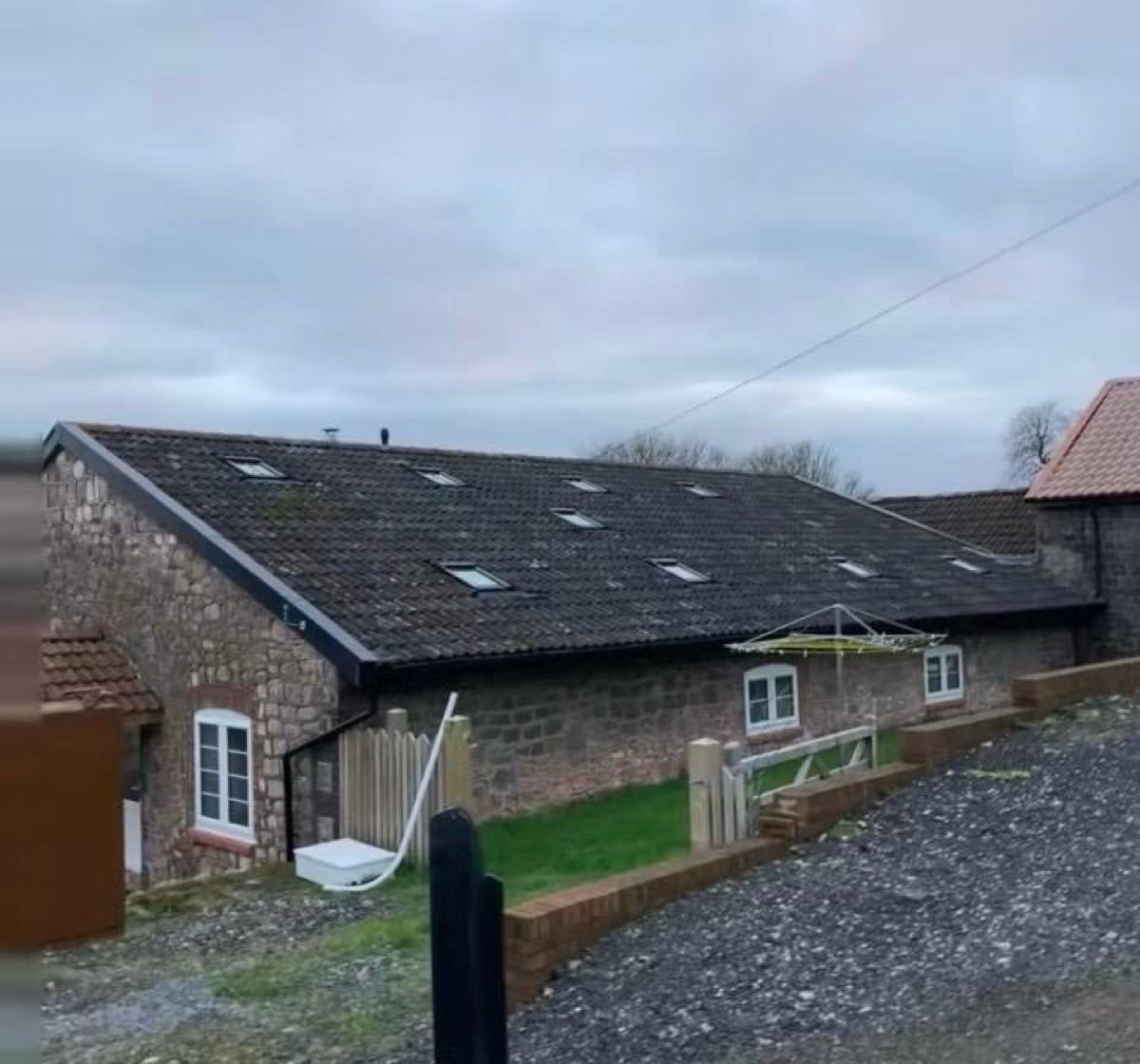 A long stone barn with new roof covering, a run of rooflights, and black fascias, soffits and guttering
